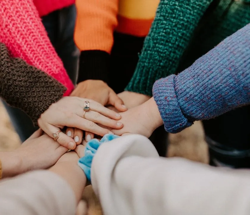 A group of people putting their hands together signalling strength as a team. 